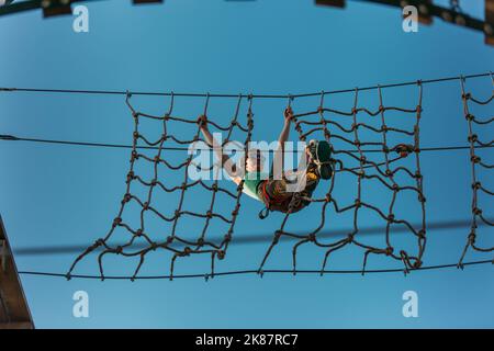 Die toughe Erwachsene Frau hängt an der Netzwand im Abenteuerpark Stockfoto