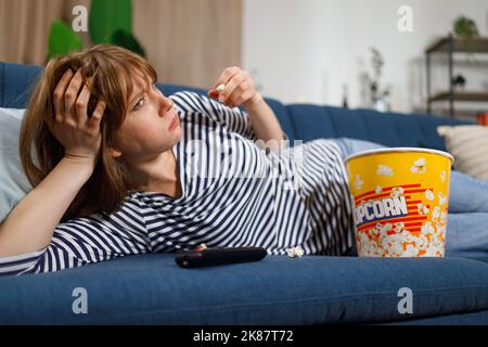 Frau schaut sich einen langweiligen Film im Fernsehen an und isst Popcorn Stockfoto