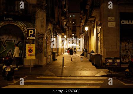 Ein Mann, der nachts in einer Seitenstraße vor der Rambla in Barcelona, Spanien, mit seinem Hund läuft Stockfoto