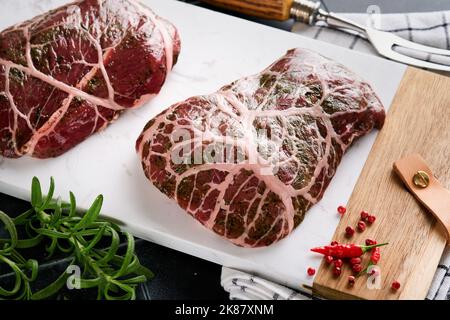 Steaks Raw. Rohes Cowboy-Steak, marmoriertes Rindfleisch mit Gewürzen Rosmarin und Pfeffer auf weißem Marmorschiefer und grauem Tischhintergrund. Draufsicht. Modell. Stockfoto