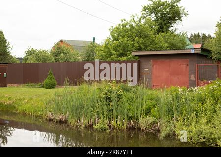 Zaun auf dem Land. Privater Bereich außerhalb der Stadt. Das Leben im Dorf. Teich in der Nähe des Hauses. Stockfoto