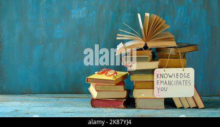 Stapel von Büchern und ein offenes Buch mit Slogan Wissen emanzipiert Sie, Lernen ist der Schlüssel zu einem besseren Leben. Freier Speicherplatz für Kopien Stockfoto