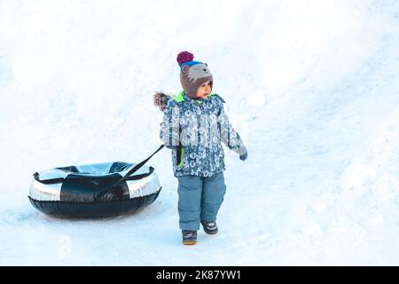 Kind mit Snow Tubing auf dem Schnee an einem sonnigen Wintertag Stockfoto