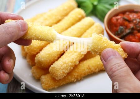 Frisch gebratene Mozzarella-Sticks brechen und Käse mit beiden Händen strecken. Stockfoto