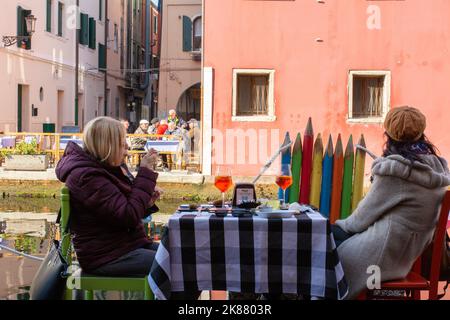 Touristen an den Tischen im Freien des Restaurants Chioggia entlang des Kanals - Chioggia, venezianische Lagune, Region Venetien, Norditalien Stockfoto