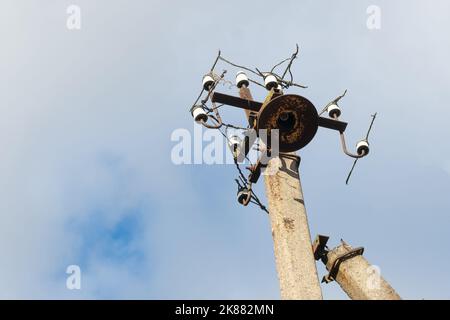 Ein alter Straßenmast aus Beton mit einem rostigen Eisenteil an der Oberseite und abgeschnittenen Drähten, Installation oder Demontage des Stromnetzes. Eine zerbrochene Energiesäule Stockfoto