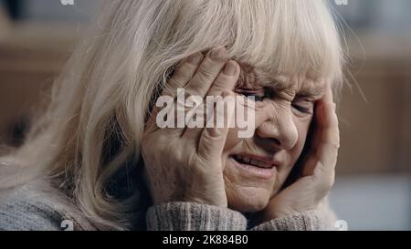 Ältere Frau mit Demenz, die an Migräne leidet und den Kopf berührt Stockfoto