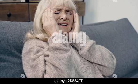Ältere Frau mit Demenz, die Kopfschmerzen hat, während sie auf dem Sofa sitzt Stockfoto