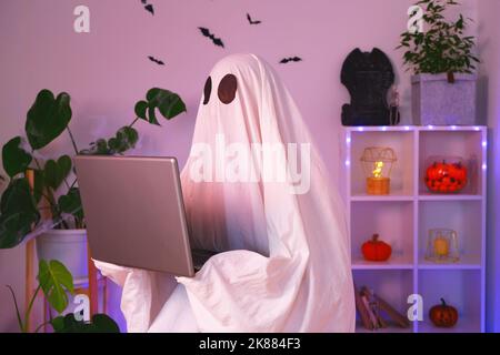 Der Geist von Halloween verwendet einen Laptop, um im Internet zu surfen, um Online-Shops, Märkte zu durchsuchen. Ein Geist macht einen Bestellcomputer für Halloween. Der Geist zahlt für einen Online-Kauf. Neonlicht. Stockfoto