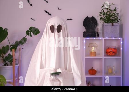 Der Halloween-Geist verwendet ein Mobiltelefon, um im Internet zu surfen, Online-Shops und Märkte zu durchsuchen. Der Geist macht an Halloween eine Bestellung von einem Smartphone. Neonlicht. Stockfoto