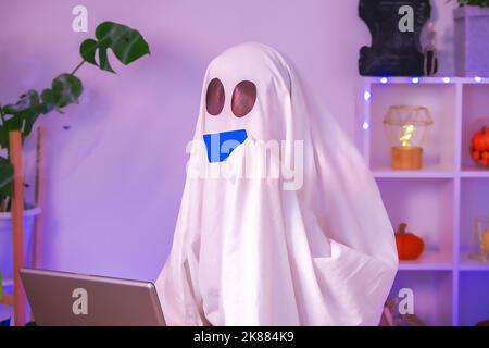 ghost of Halloween nutzt Laptop im Internet surfen, Online-Shops durchsuchen, Märkte. Ein Geist macht eine Bestellung vom Computer für Halloween. Ghost zahlt für den Online-Kauf per Kreditkarte. Neonlicht. Stockfoto