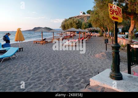 Mann fotografiert Strand, Windmühle und hübsche weiße Katze auf einem Bettstuhl, Anaxos. Lesbos. Wassersport-Schild. September/Oktober 2022. Herbst. Stockfoto