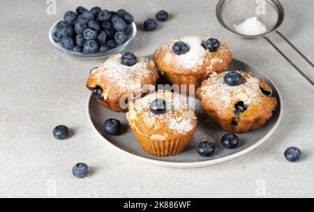 Hausgemachte Muffins mit Heidelbeere und Mandeln bestreut mit Puderzucker auf dem Teller auf grauem Hintergrund Stockfoto