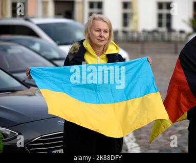 Wismar, Deutschland. 21. Oktober 2022. Eine Frau mit der Nationalflagge der Ukraine steht bei einer Mahnwache auf dem Marktplatz von Wismar. Nach dem Brand in einem Flüchtlingsheim im Nordwesten Mecklenburgs wollen die Menschen in Wismar ein Zeichen der Solidarität für Flüchtlinge aus der Ukraine und anderen Ländern setzen. Quelle: Frank Hormann/dpa/Alamy Live News Stockfoto