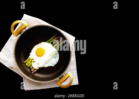 Spiegelei und Spargel in einer Pfanne auf schwarzem Hintergrund Stockfoto