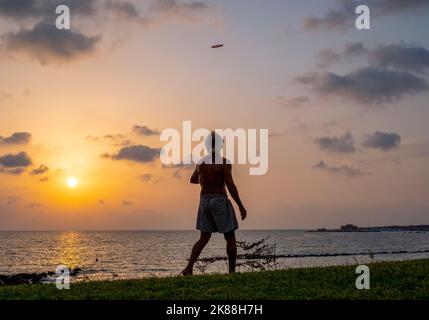 Ein Mann, der an einem Strand trainiert und eine Frisbee wirft, Paphos, Zypern. Stockfoto