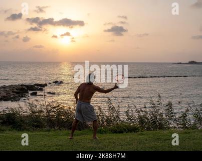 Ein Mann, der an einem Strand trainiert und eine Frisbee wirft, Paphos, Zypern. Stockfoto