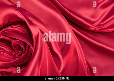 Rote Seide Satin Hintergrund Nahaufnahme. Luxuriöser, reicher Hintergrund mit gefaltetem und verdrehtem Seidenstoff. Valentinstag, Weihnachten, Jubiläum, Schwarzer Freitag. Webbann Stockfoto