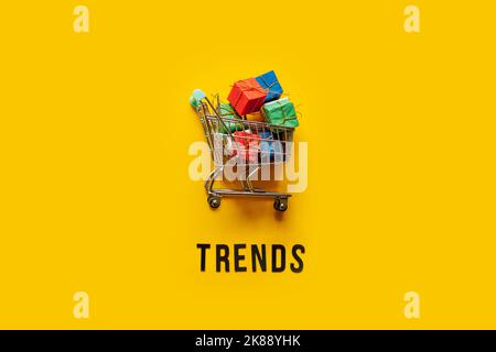ECommerce Retail Shopping Trends Konzept. Word Trends und Mini-Warenkorb mit Box auf gelbem Hintergrund. Stockfoto