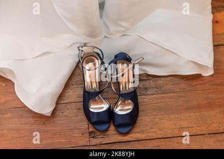 Blick von oben auf die offenen Schuhe der Braut sind entschnallt und neben dem Hochzeitskleid angelegt. Stockfoto