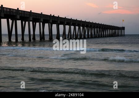 Die Sonne geht über dem Pensacola Pier auf, während die Wellen vom Golf von Mexiko auf den Sand des Strandes an der Golfküste fließen Stockfoto