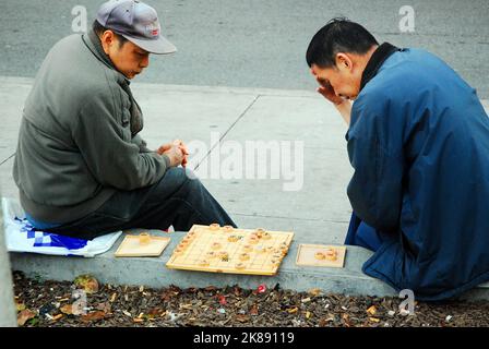 Zwei ältere asiatische Männer betrachten ihren nächsten Schritt bei einem Spiel im Freien mit Xiangqi in einem Park außerhalb der Stadt Stockfoto