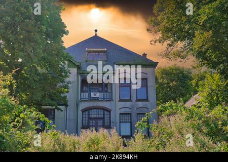 Gruseliges Spukhaus inmitten von Bäumen unter einem feurigen Himmel-Konzept Stockfoto