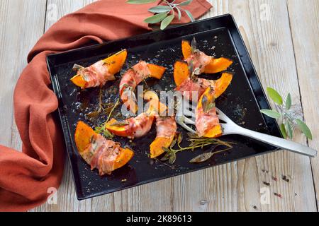 Hokkaido-Kürbislücken, eingewickelt in Speck mit Salbeiblättern und Thymian, in Olivenöl mit Pfeffer und Salz gebacken Stockfoto