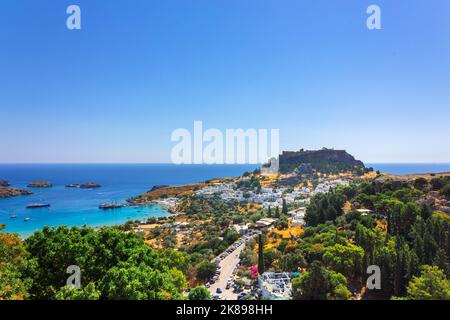 Panoramablick auf den farbenfrohen Hafen im Dorf Lindos und auf die Akropolis von Rhodos. Luftaufnahme der schönen Landschaft, alten Ruinen, Meer mit Segelbooten und Küste der Insel Rhodos in der Ägäis Stockfoto