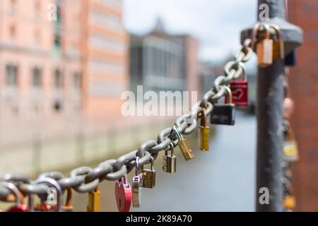 An einer alten Gliederkette der Speicherstadt in Hamburg hängen viele bunte sogenannte Liebesschlösser in verschiedenen Formen. Die Kette hebt sich von der ab Stockfoto