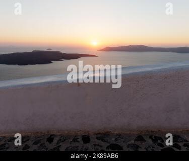 Sonnenuntergang über Thirasia von einem Küstenpfad in Fira. Die griechische ägäische Kykladen-Insel Santorin. Stockfoto