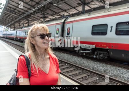 Reife Erwachsene Frau mit Sonnenbrille wartet auf Zug auf Plattform Stockfoto