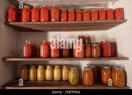 Holzregale auf der Sauer-Beckmann Living History Farm mit hausgemachten Tomaten, Salsa, Sauerkraut, Okra und Karotten in Kugelgläsern. Stockfoto