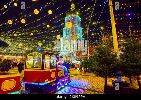 KIEW, UKRAINE - 28. DEZEMBER 2021: Geschmückter Sophia-Platz mit überfülltem Weihnachtsmarkt, Hauptweihnachtsbaum, reitendem Touristenzug und Hagia Sophia-Chata Stockfoto
