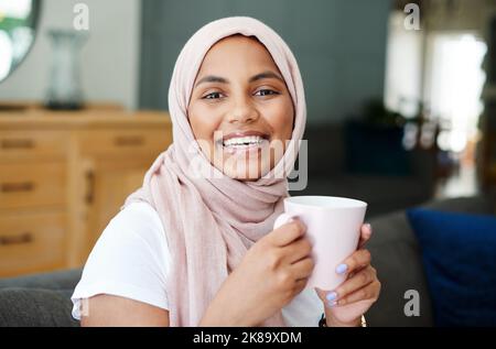 Es gibt nichts Vergleichbares wie ein Pick-me-up in einer Tasse. Eine attraktive junge Frau, die allein auf ihrem Sofa zu Hause sitzt und eine Tasse Kaffee genießt. Stockfoto