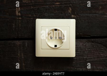 Eine weiße Steckdose auf einem alten verbrannten Holzbrett an der Wand eines Hauses in Nahaufnahme Stockfoto