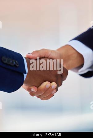 Sie haben es gut gemacht und deshalb haben Sie es verdient. Zwei unkenntliche Geschäftsleute, die sich in einem modernen Büro die Hände schütteln. Stockfoto