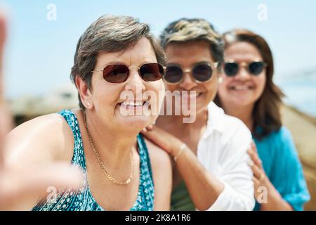 Altern ist unvermeidlich, aber man muss nicht alt sein. Eine reife Gruppe von Freunden stehen zusammen und posieren für ein Selfie während eines Tages am Strand. Stockfoto