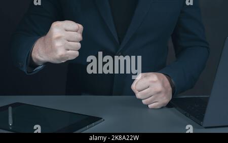 Geschäftsmann schlägt Faust auf den Tisch, zugeschnittenes Bild. Wütend Geschäftsmann zeigt seine Fäuste. Mann mit geballter Faust auf dem Schreibtisch. Chef zusammenhält seine Fäuste in ra Stockfoto