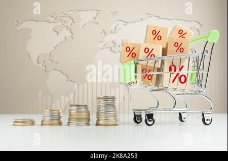 Inflation in der globalen Krise und steigende Preise. Kleiner Warenkorb mit gestapelten Münzen und World Cost Rising Konzept. Prozentsatz Würfel im Supermarkt Troll Stockfoto