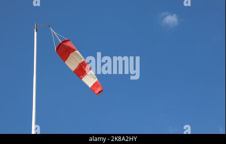 Wetterfahne in Weiß und Rot, um die Richtung anzuzeigen, aus der der Wind weht, auf einem hellblauen Stockfoto