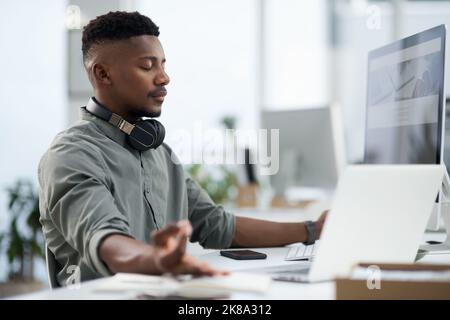 Atmen Sie ein, atmen Sie aus. Ein junger Mann, der bei der Arbeit meditiert. Stockfoto