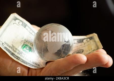 amerikanische Dollar und eine Glaskugel des Planeten liegen in den Händen einer alten Frau, Finanzwelt und Menschen Stockfoto