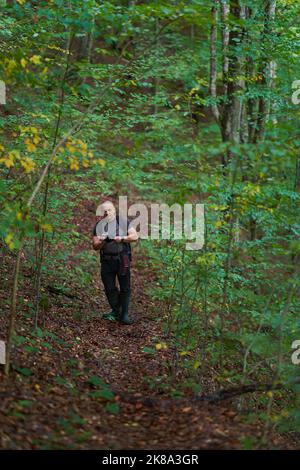 Erfahrener Wanderer, der sich auf einem Wanderweg durch einen alten, üppigen Wald schlenderte Stockfoto