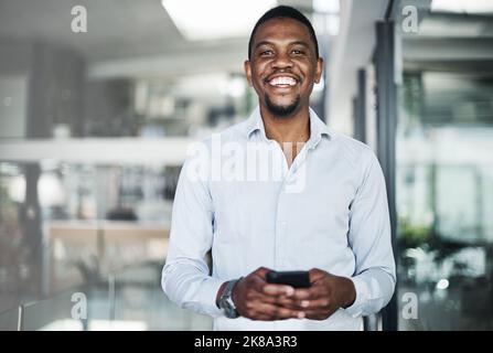Mein Geschäft ruht in meiner Hand. Ein hübscher junger Geschäftsmann, der alleine im Büro steht und tagsüber sein Handy benutzt. Stockfoto