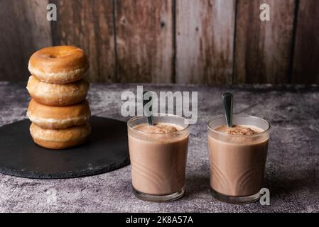 Zwei Gläser Milch mit Kakao mit vier glasierten Donuts auf einem Steinteller. Stockfoto