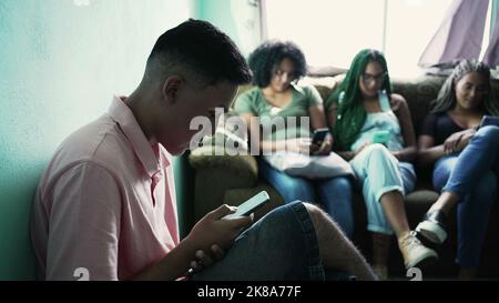 Ein hispanischer Mann, der im Vordergrund auf das Mobiltelefon schaut. Drei weibliche schwarze Freundinnen im Hintergrund mit Telefonen Stockfoto