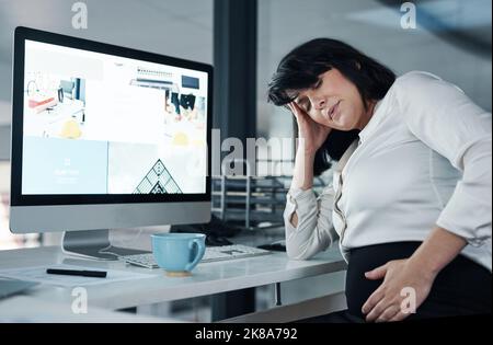 Mein Baby hört heute nicht mehr auf zu treten. Eine attraktive, Schwangere, die allein im Büro sitzt und unter Bauchschmerzen leidet. Stockfoto