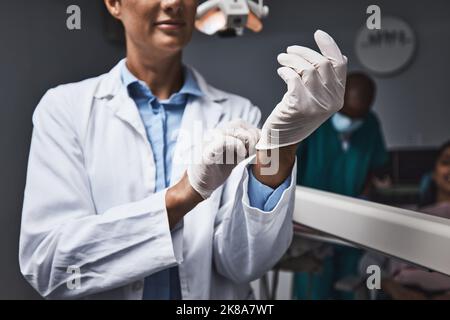 Ihr Lächeln ist in sicheren Händen. Ein nicht erkennbarer Zahnarzt legt Handschuhe an, um einen chirurgischen Eingriff vorzubereiten. Stockfoto