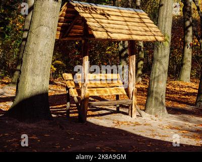 Hölzerne überdachte Bank zwischen Baumstämmen in einem Herbstpark Stockfoto